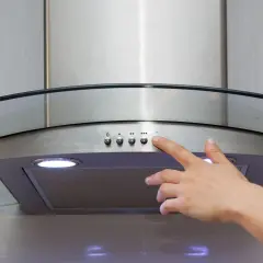 Main d'une personne appuyant sur le bouton d'une hotte recyclage ou évacuation moderne en acier inoxydable avec un éclairage intégré.