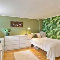 Chambre avec mur végétal, lit blanc, commode et télévision.