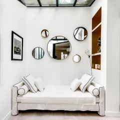 Plusieurs miroirs ronds de tailles variées sont accrochés sur un mur blanc au-dessus d'un canapé blanc.
