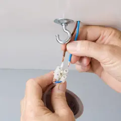Mains électriques connectées pour changer un lustre. Un crochet au plafond supporte le nouveau luminaire.
