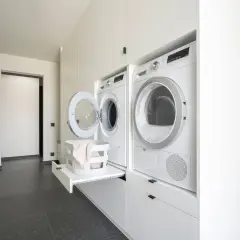 Buanderie pratique avec lave-linge et sèche-linge blancs, panier à linge escamotable et rangements intégrés.