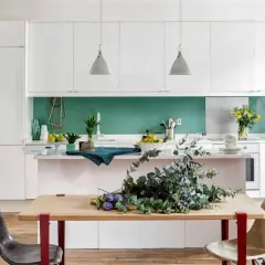 Table en bois avec des branches d'eucalyptus et des chaises, devant une cuisine moderne avec un mur vert vif. Une belle deco salle a manger.