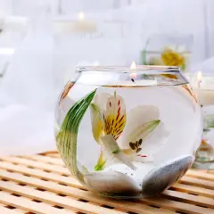 Comment décorer un grand vase en verre transparent : une fleur blanche flottante, des galets et une bougie allumée créent une ambiance zen.