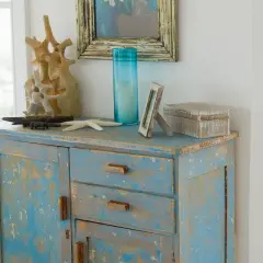 Meuble patiné bleu délavé, orné d'objets marins et d'une boîte décorative.