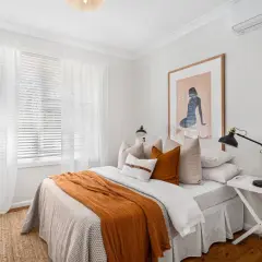 Lit douillet avec jeté orange, coussins et tableau abstrait.