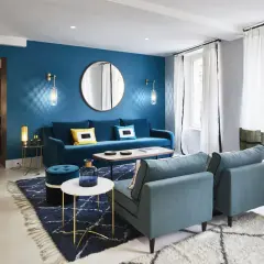 Salon moderne aux murs bleu paon, avec canapé velours, fauteuils assortis, tapis graphique et éclairage tamisé.