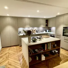 Cuisine moderne avec îlot central, table intégrée, rangements et parquet en chevrons.