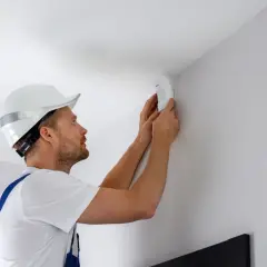 Un technicien installe un détecteur de mouvement 5 fils au coin d'un mur blanc.