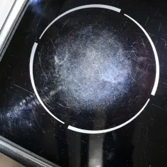 Gros plan sur une plaque à induction noire, marquée par de nombreuses rayures sur la zone de cuisson.