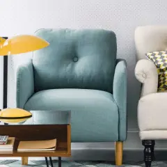 Fauteuil confortable couleur aqua, à côté d'un autre fauteuil crème avec un coussin géométrique. Une lampe jaune et une table basse en bois complètent la scène.