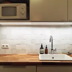 Cuisine blanche épurée avec crédence en zellige texturé, plan de travail en bois, évier et robinetterie modernes.
