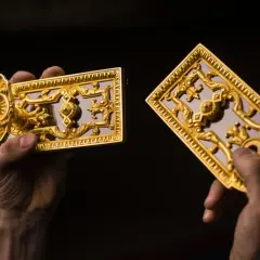 Mains tenant des ornements dorés, peut-être du bronze ou du laiton, aux motifs complexes.
