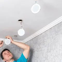 Un homme installe de nouvelles suspensions rondes au plafond, remplaçant les anciens spots.