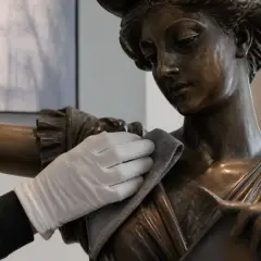 Une main gantée nettoie délicatement un buste en bronze. Le bicarbonate de soude est un excellent produit pour nettoyer le bronze.