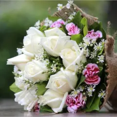 Un bouquet de roses blanches et de petites fleurs roses, en forme de vase, est emballé dans de la toile de jute.