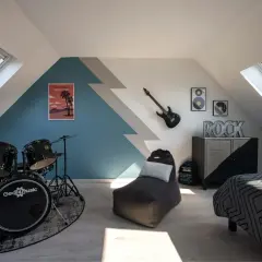 Chambre d'ado avec batterie, guitare électrique, pouf et lit décoré.