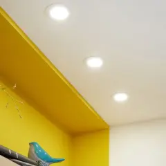 Disposition de spots encastrés au plafond pour une ambiance lumineuse dans la chambre, éclairant joliment les étagères jaunes.