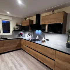Cuisine moderne avec meubles en bois, plan de travail gris et hotte noire.