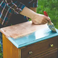 Une personne ponce un meuble vernis pour le repeindre en bleu sarcelle.