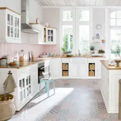 Une cuisine blanche style campagne chic, lumineuse avec ses grandes fenêtres, son plan de travail en bois et son sol aux motifs colorés.