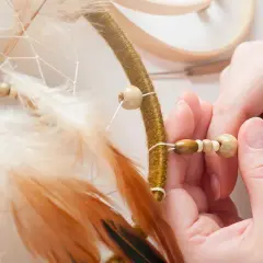 Mains assemblant un attrape-rêves, ajoutant des perles en bois pour une touche naturelle. Idées pour que faire avec des perles en bois.