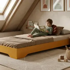 Enfant lisant un livre dans une chambre mansardée avec un lit bas et une fenêtre de toit.