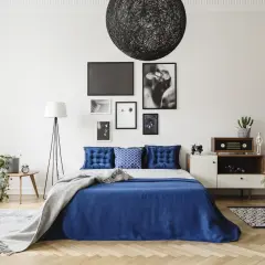 Chambre bleu nuit avec lit, coussins capitonnés, plaid gris, lampadaire, table de chevet et décoration murale.