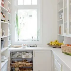 Arrière-cuisine blanche avec étagères remplies, fruits et légumes sur le comptoir.