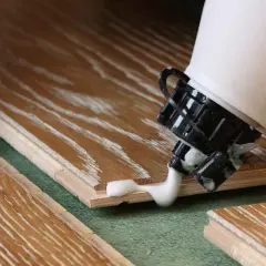 Application de colle à bois sur des lames de parquet. La colle blanche coule de l'embout d'une bouteille sur le bois.