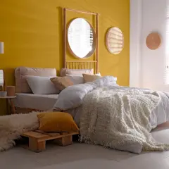 Chambre de fille avec mur jaune, lit blanc, tapis shaggy et miroir rond.