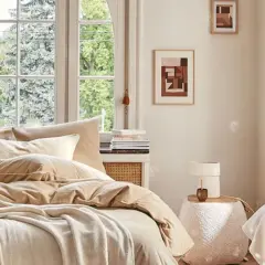 Lit douillet aux tons neutres, avec coussins, plaid et vue sur jardin par la fenêtre.