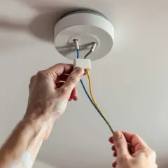 Mains électriques connectées pour installer un plafonnier. Les fils colorés sont manipulés avec soin.