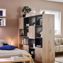 Chambre et salon séparés par une étagère modulable, avec lit douillet et canapé rayé.