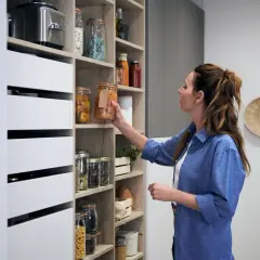Une femme range son aménagement cellier, plaçant un bocal de conserves sur une étagère bien organisée.