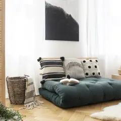 Futon vert foncé avec coussins décoratifs, panier en osier et tableau abstrait.