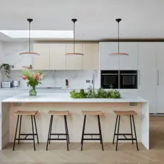 Une cuisine moderne et lumineuse, parfaite pour imaginer sa cuisine de rêve. Îlot central avec tabourets, armoires épurées et plantes aromatiques.