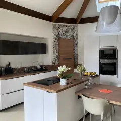 Cuisine moderne avec des meubles blancs et un **crédence et plan de travail assortis** en bois. Une orchidée blanche décore l'îlot central.