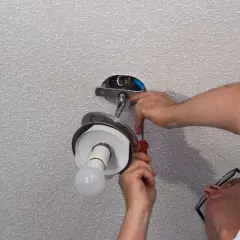 Un homme installe un lustre au plafond, utilisant un tournevis pour fixer le luminaire.