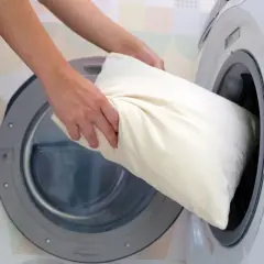 Une personne met un oreiller blanc dans une machine à laver.