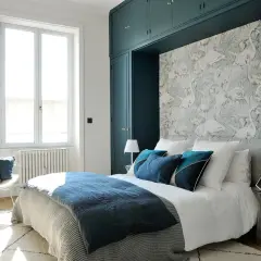 Chambre avec papier peint flamants roses, lit bleu marine et armoire vert foncé.