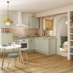 Cuisine moderne et colorée avec des meubles verts, une table ronde et des étagères décorées.