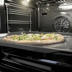 Une pizza garnie sur une plaque dans un four pyrolyse Siemens. La pizza est prête à être cuite.