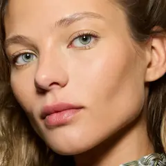 Un visage de femme aux yeux verts, peau lumineuse. Comment reconnaître du bronze ? La peau de ce modèle a un éclat naturel, comme si elle était hâlée par le soleil.