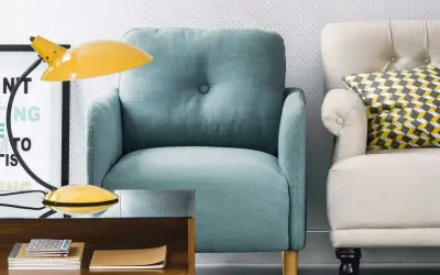 Fauteuil confortable couleur aqua, à côté d'un autre fauteuil crème avec un coussin géométrique. Une lampe jaune et une table basse en bois complètent la scène.
