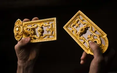 Mains tenant des ornements dorés, peut-être du bronze ou du laiton, aux motifs complexes.