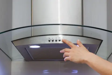Main d'une personne appuyant sur le bouton d'une hotte recyclage ou évacuation moderne en acier inoxydable avec un éclairage intégré.