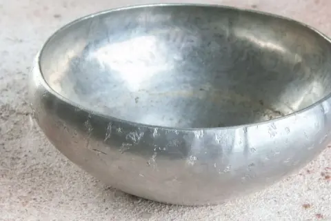 Bol en étain usé, posé sur une surface texturée.