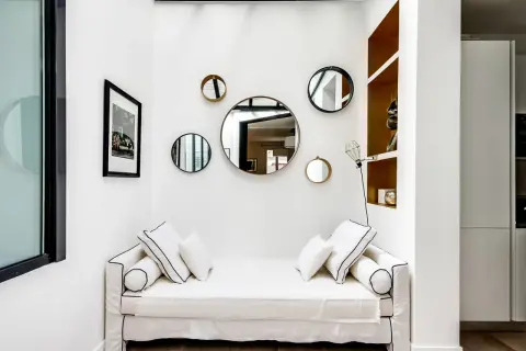 Plusieurs miroirs ronds de tailles variées sont accrochés sur un mur blanc au-dessus d'un canapé blanc.