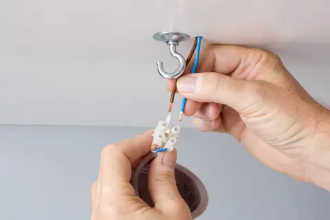 Mains électriques connectées pour changer un lustre. Un crochet au plafond supporte le nouveau luminaire.