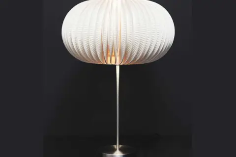 Lampe avec abat-jour sphérique en carton blanc plissé, sur pied métallique.